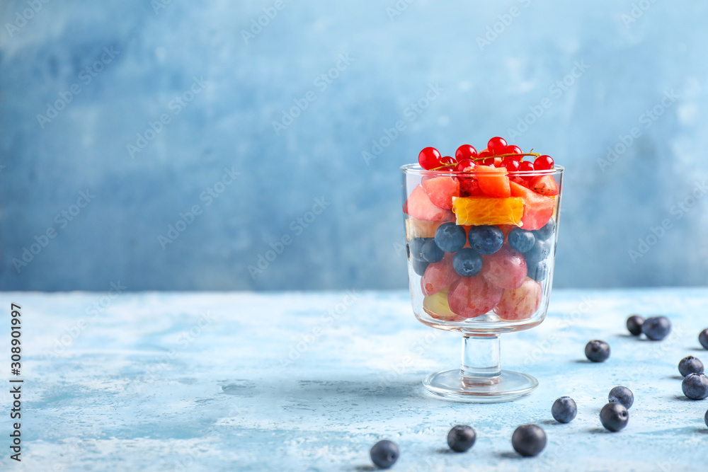 Glass with tasty fruit salad on color background