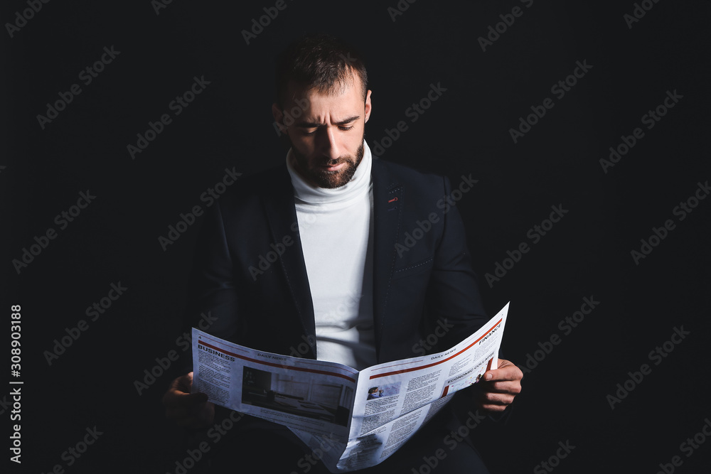 Portrait of stylish young man reading newspaper on dark background