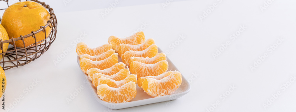 Beautiful peeled tangerines in a plate and metal basket isolated on bright white clean table in a mo