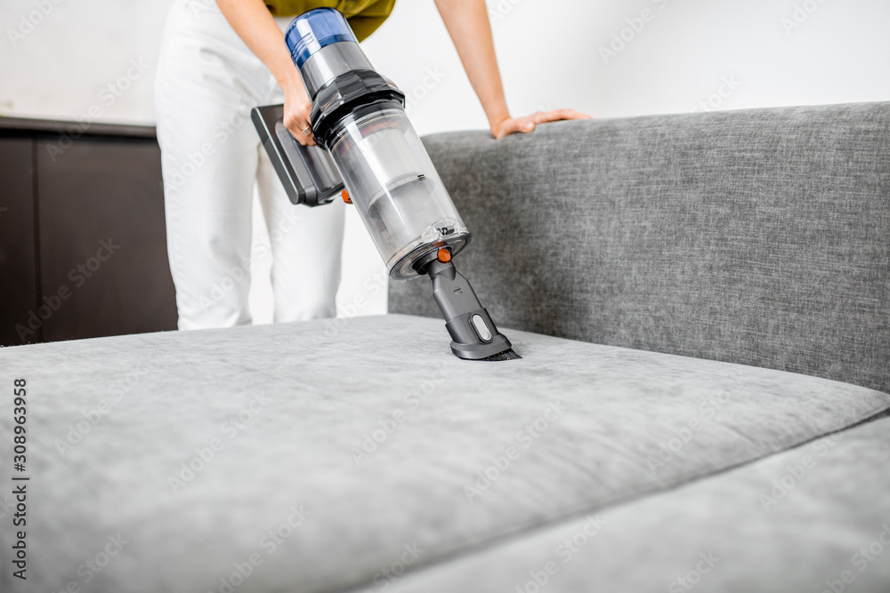 Woman cleaning sofa with a modern cordless vacuum cleaner with a special nozzle, close-up. Dry clean