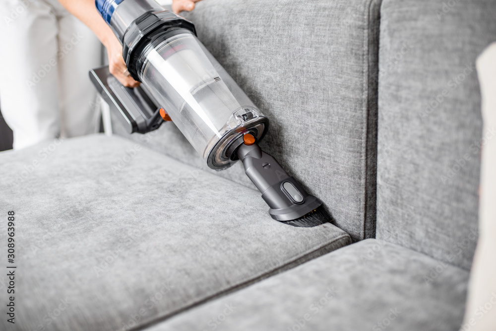 Woman cleaning sofa with a modern cordless vacuum cleaner with a special nozzle, close-up. Dry clean