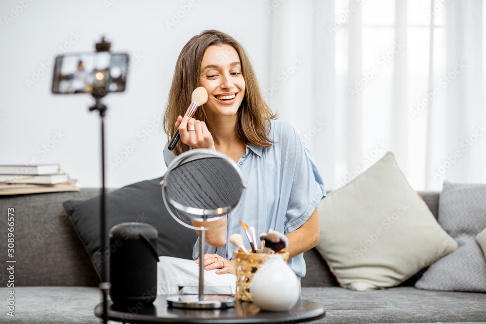 Young woman recording on a smart phone her vlog about cosmetics, showing and demonstrating makeup. I