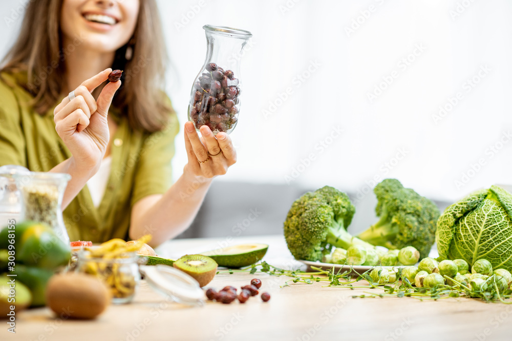 Portrait of a young cheerful woman with dried rosehip and lots of healthy green food on the table. C