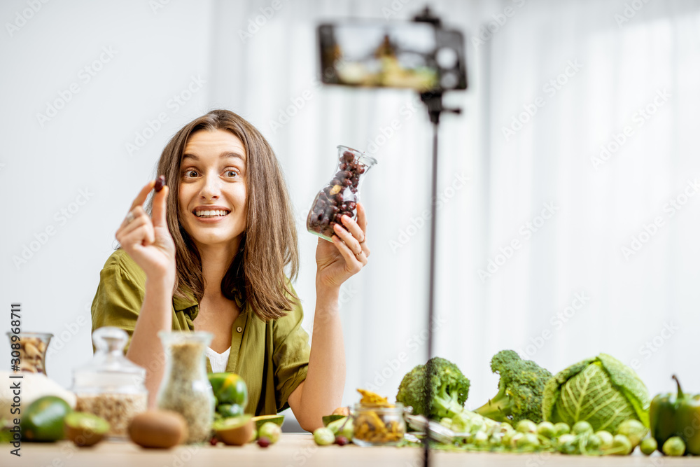 一位年轻女士用智能手机录制了她关于健康饮食的视频日志。坐在桌子旁。