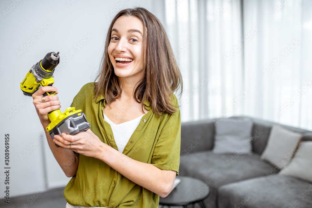 Portrait of a young and happy handywoman with cordless screwdriver at home. Concept of an easy house