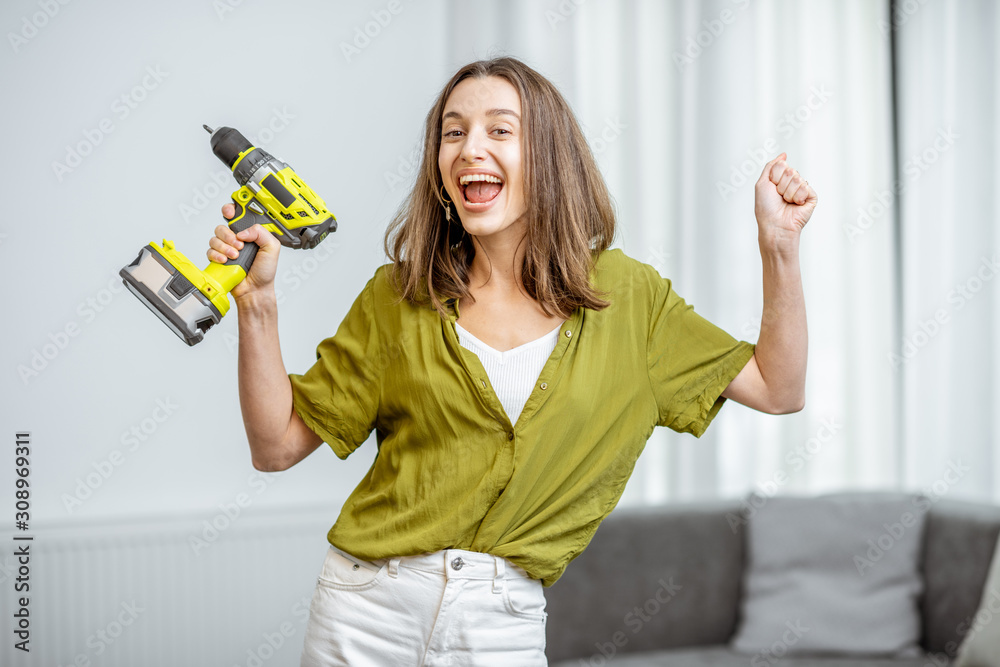 Portrait of a young and happy handywoman with cordless screwdriver at home. Concept of an easy house