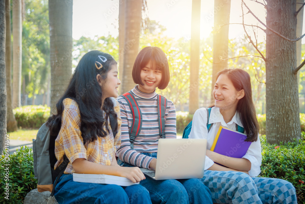 三名亚洲青少年学生坐在公园里一起用笔记本电脑做作业