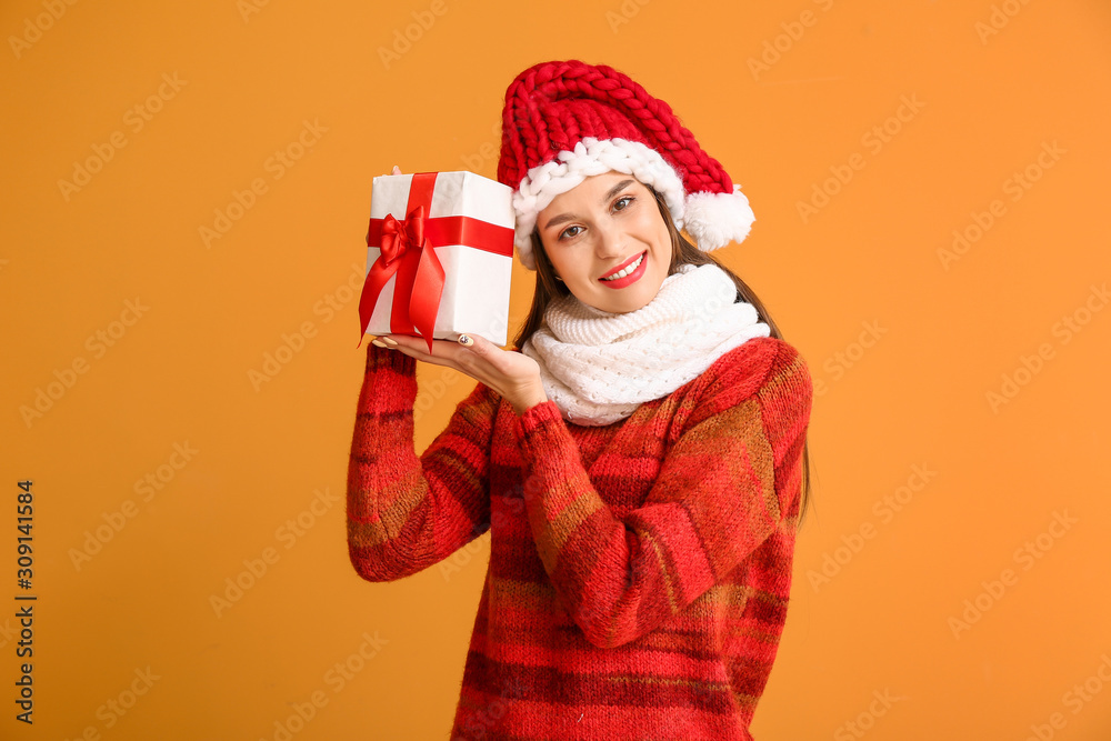 Happy young woman in winter clothes and with Christmas gift on color background