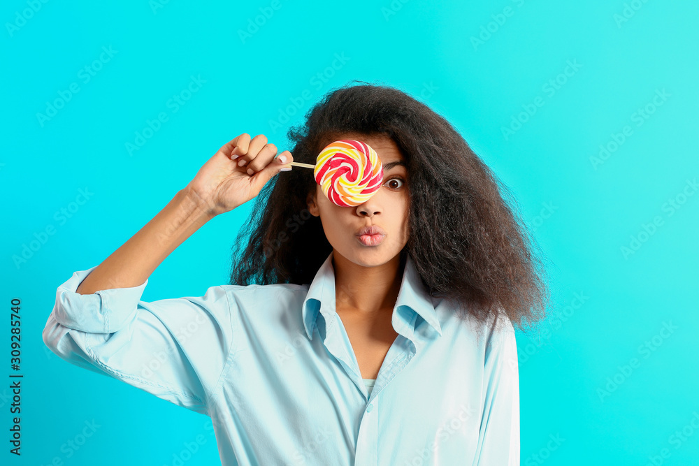 Surprised African-American woman with tasty lollipop on color background