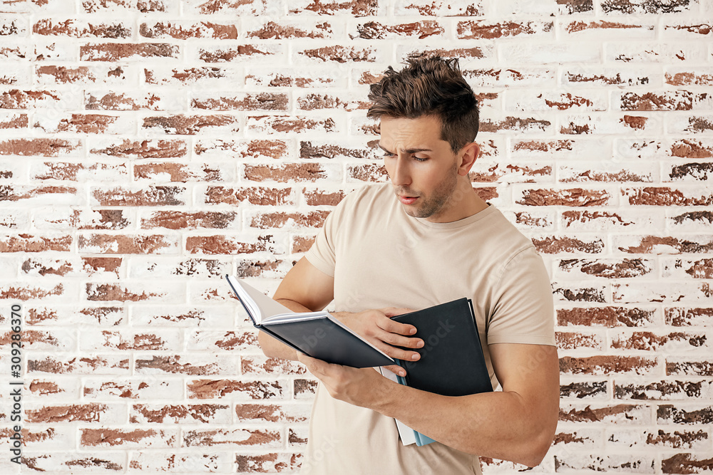 Handsome young man reading books near brick wall