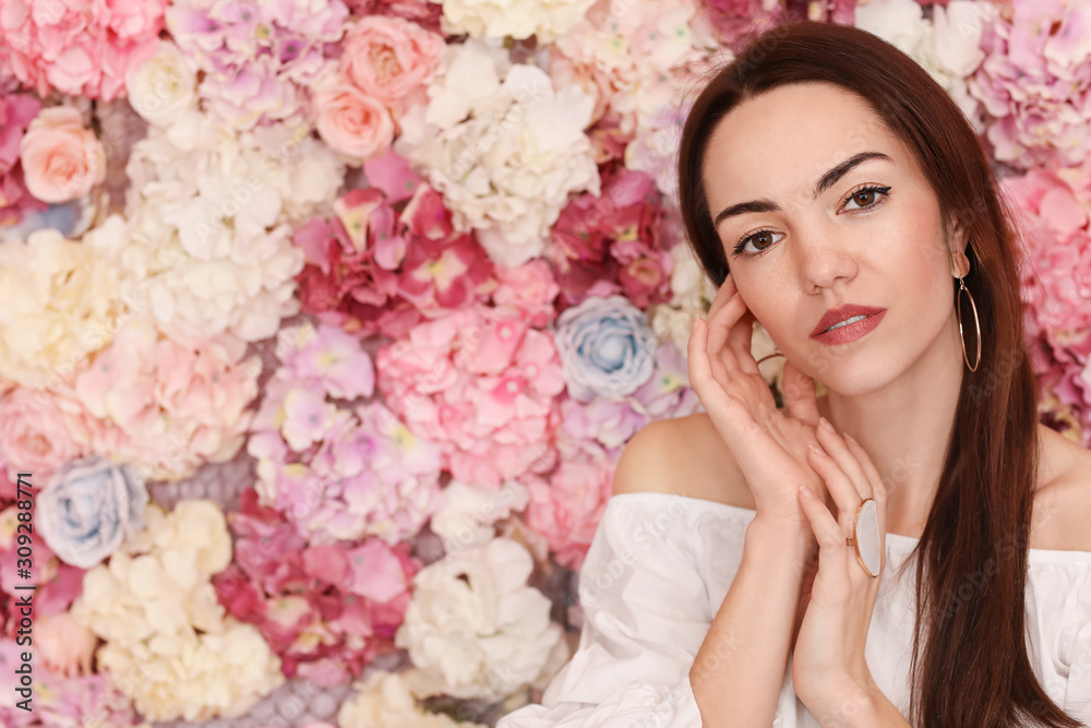 Portrait of beautiful young woman near wall made of flowers