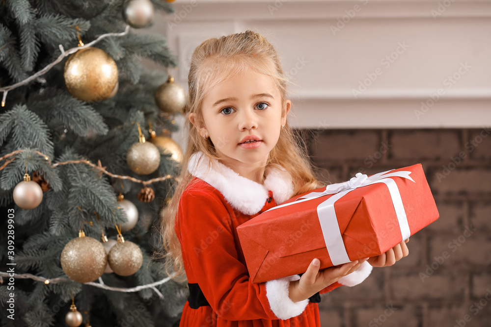 Cute little girl in Santa costume and with Christmas gift at home