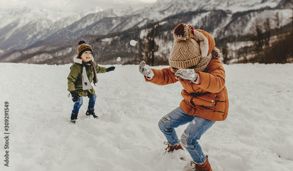 happy kids boy and girl playing snowballs on  walk