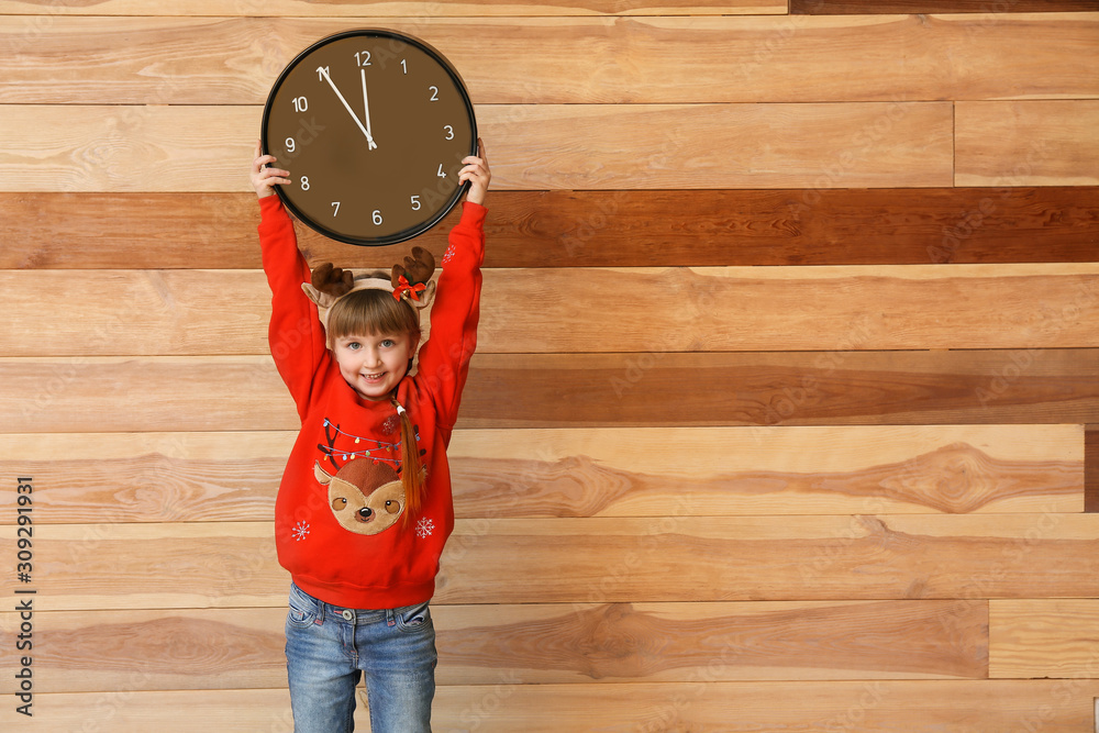 Little girl with clock on wooden background. Christmas countdown concept