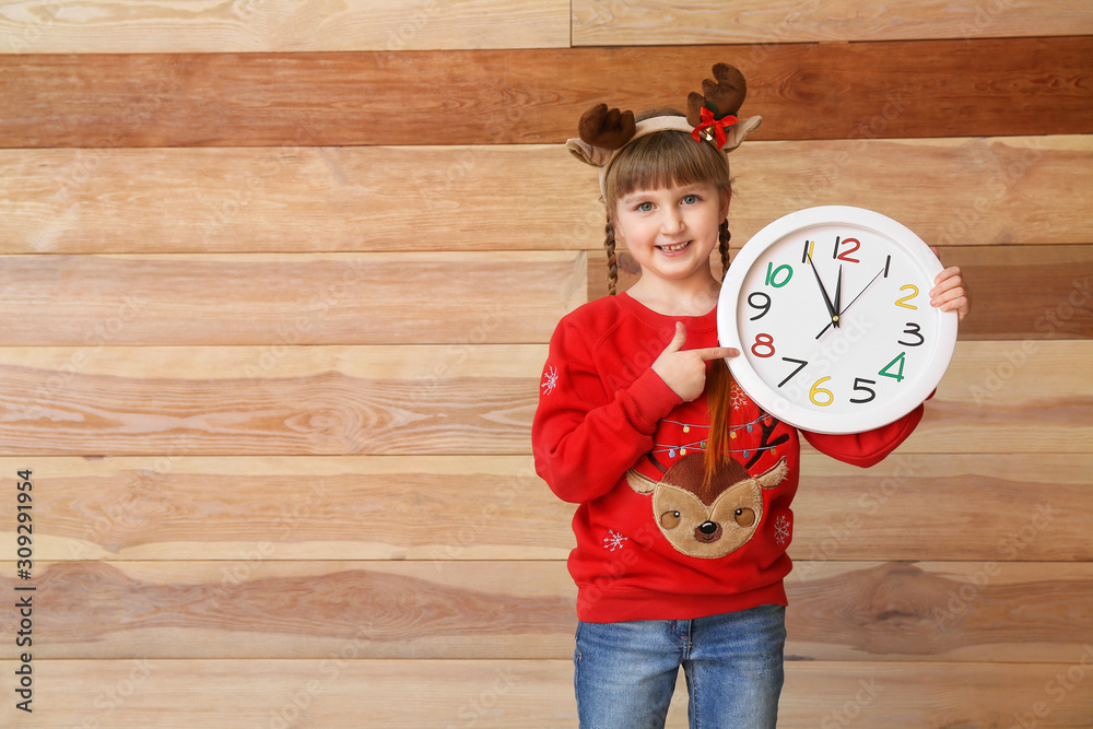 Little girl with clock on wooden background. Christmas countdown concept