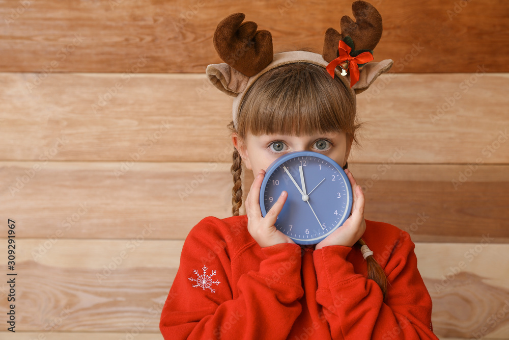 Little girl with alarm clock on wooden background. Christmas countdown concept