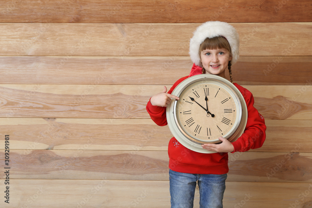 Little girl with clock on wooden background. Christmas countdown concept