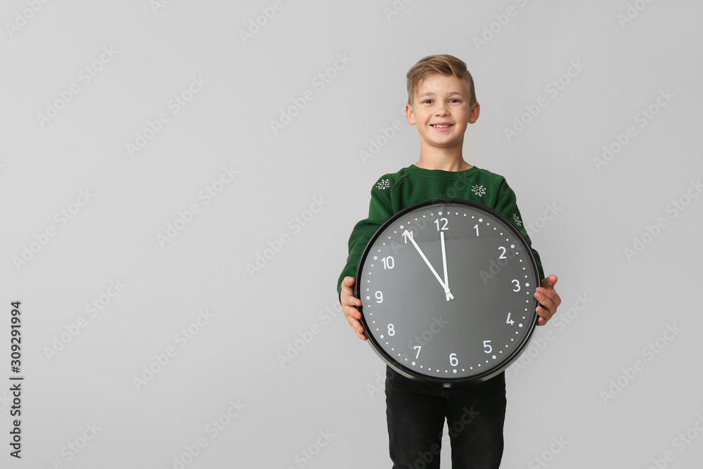 Little boy with clock on light background. Christmas countdown concept