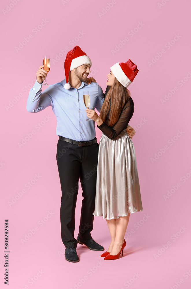 Happy couple in Santa Claus hats and with glasses of champagne on color background