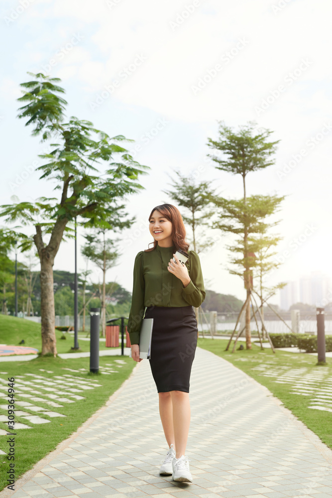 Young successful asian female going to work with cup of take away coffee