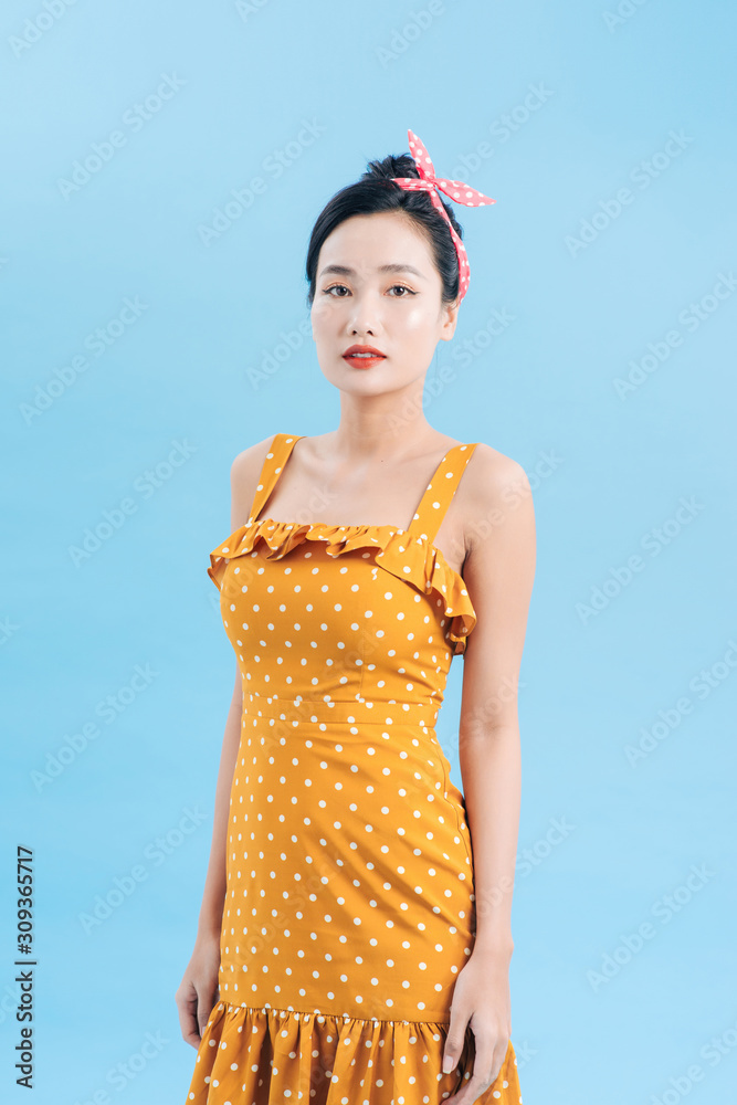 Young beautiful woman posing in new casual yellow and white dotted dress on a blue background