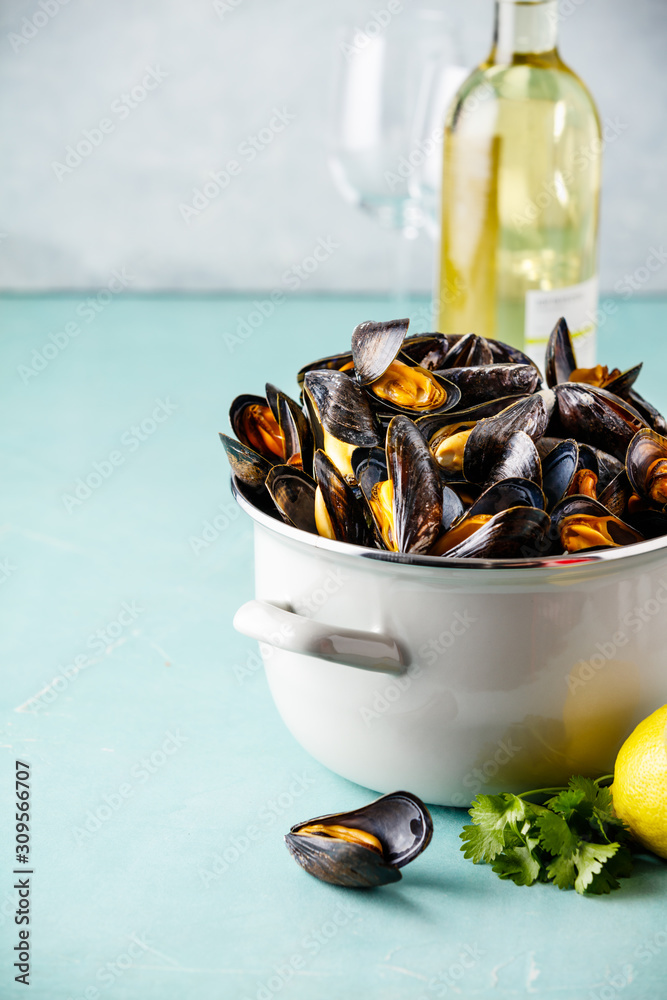 Pot of steamed mussels with lemon, herbs and white wine on blue background