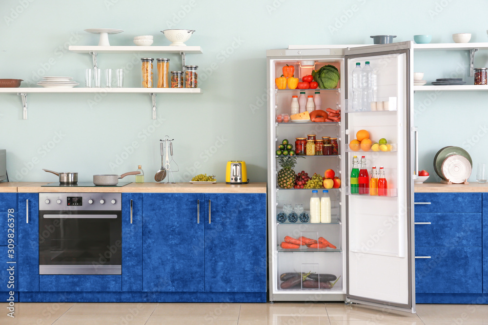 Open big fridge with products in interior of kitchen