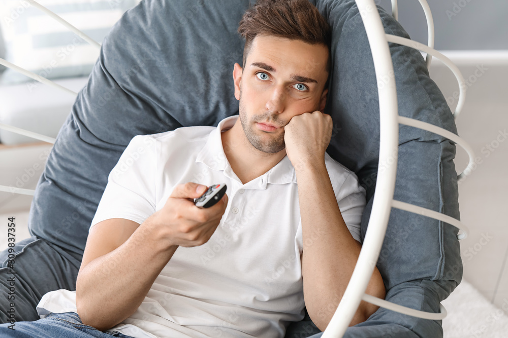 Bored man watching TV while sitting in armchair at home