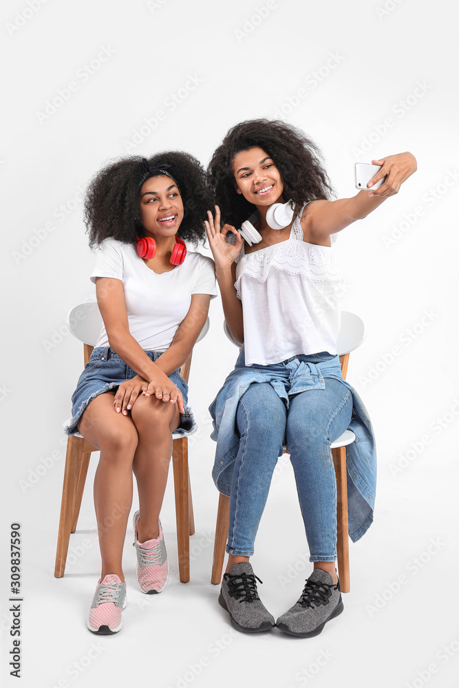 Portrait of young African-American women taking selfie on white background