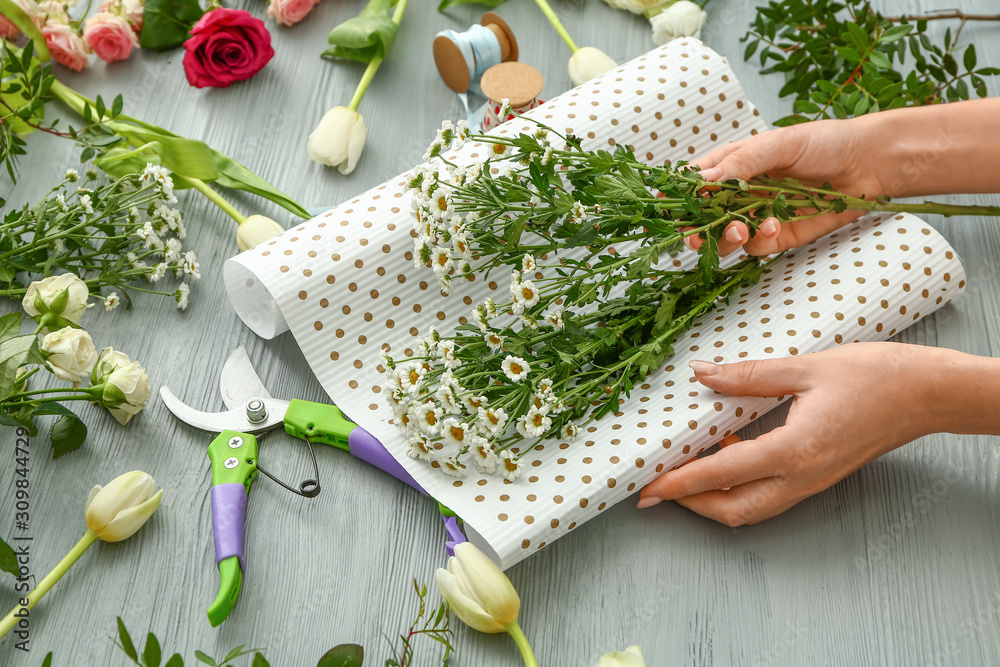 Female florist making beautiful bouquet on grey background