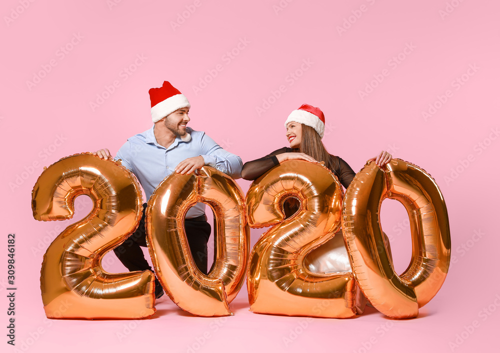 Happy couple in Santa Claus hats and with air balloons on color background