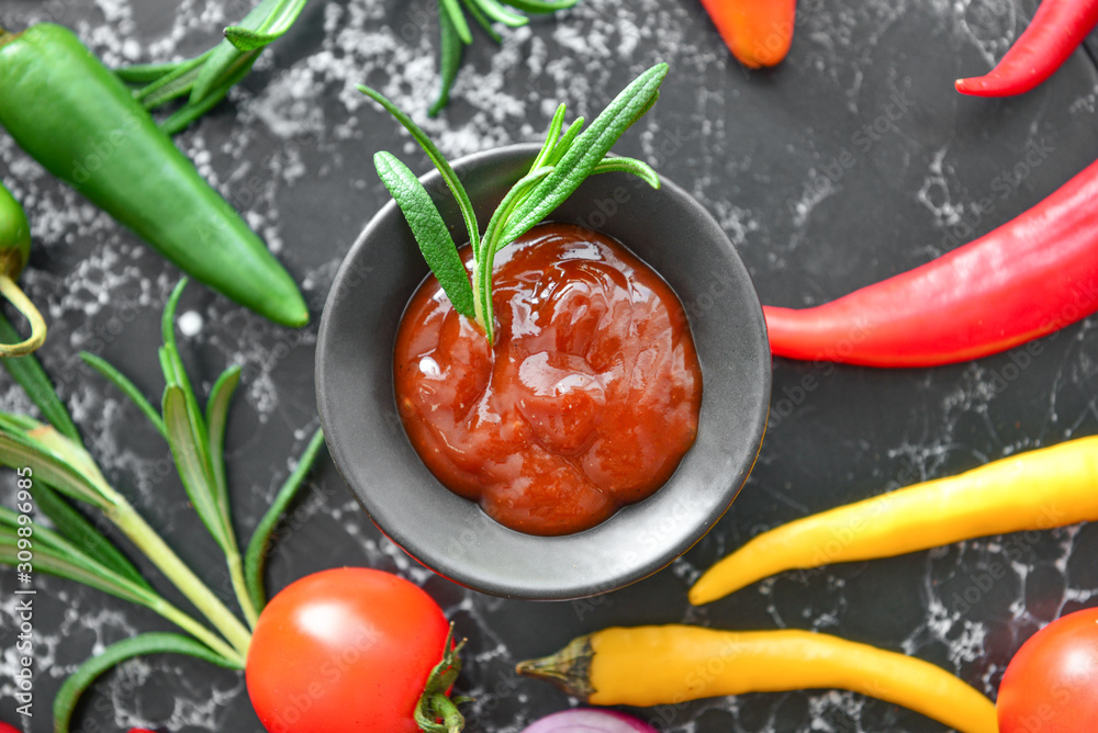 Bowl with barbecue sauce and vegetables on dark table