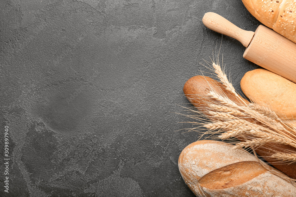 Assortment of fresh bread with rolling pin on dark background