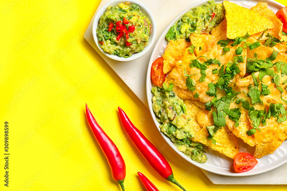 Board with tasty nachos and guacamole on color background