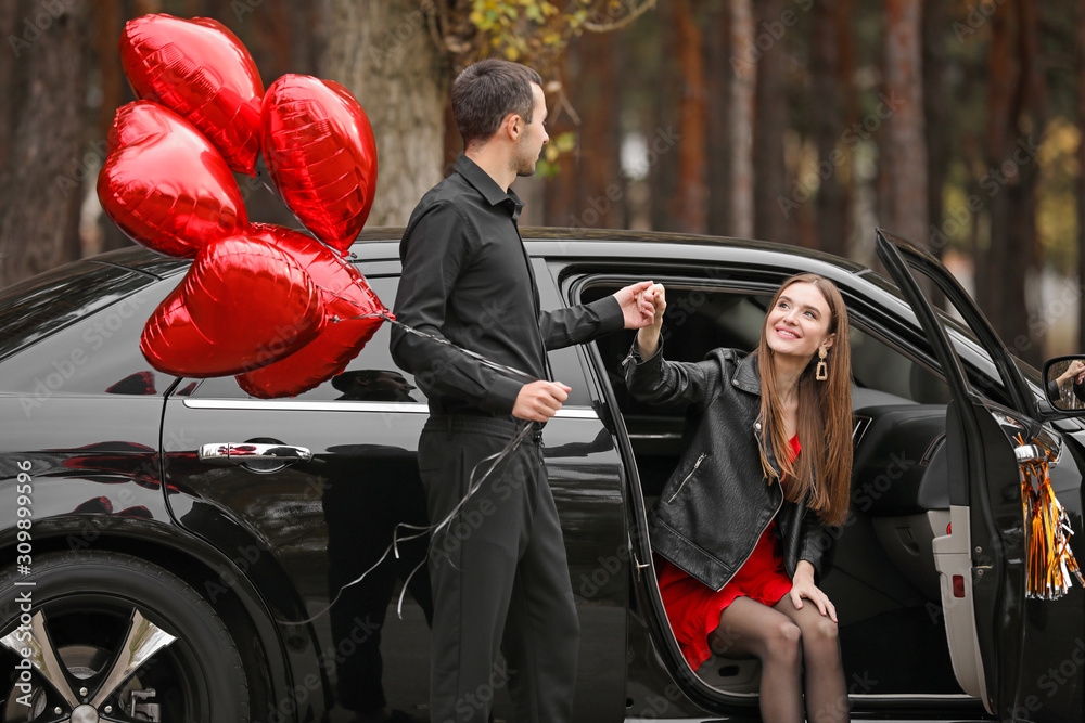 Man with air balloons helping his girlfriend to get out of car. Valentines Day celebration