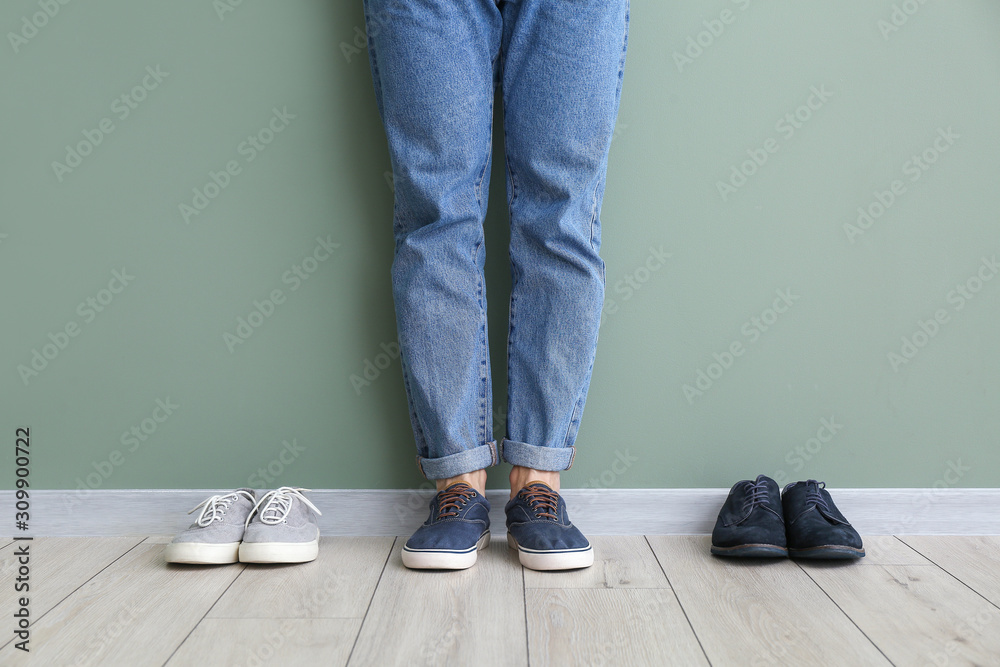 Young man with different stylish shoes near color wall