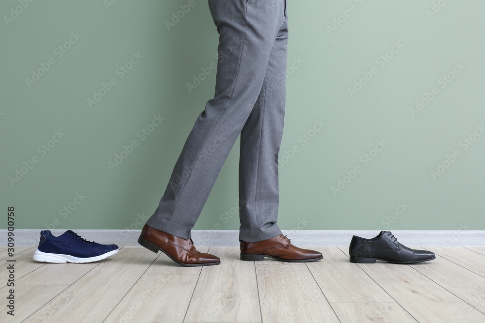 Young man with different stylish shoes near color wall