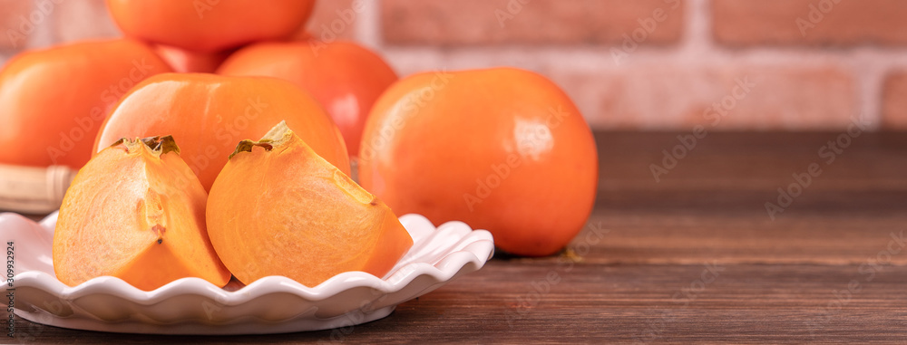 Fresh beautiful sliced sweet persimmon kaki on dark wooden table with red brick wall background, Chi