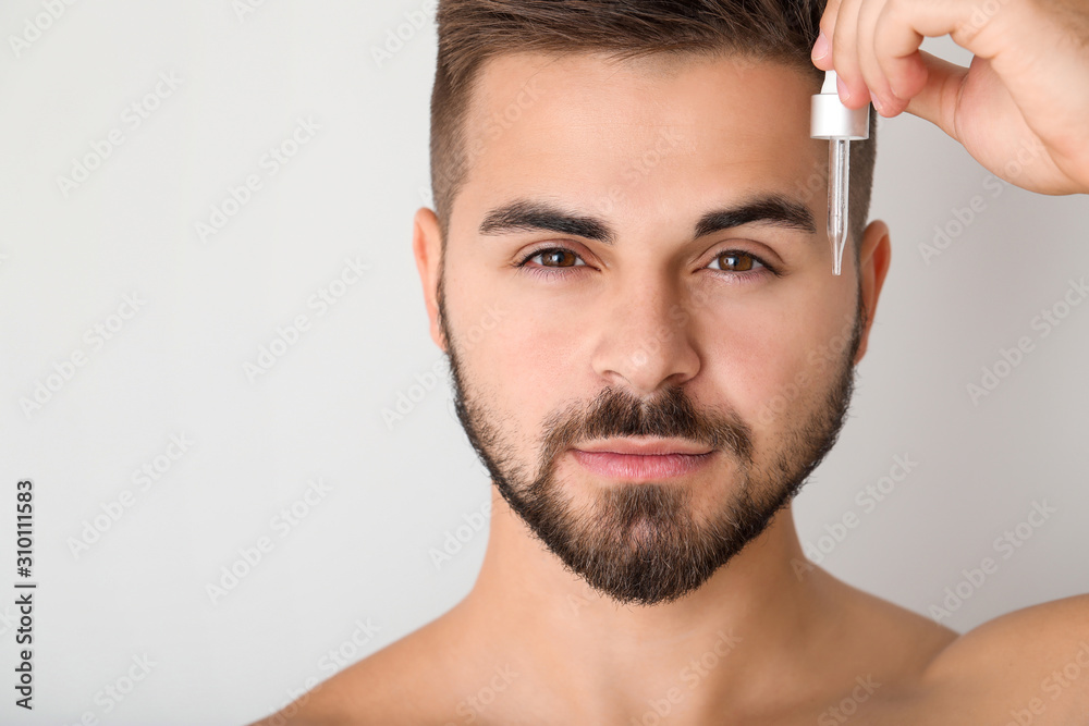 Handsome young man with cosmetic product on light background