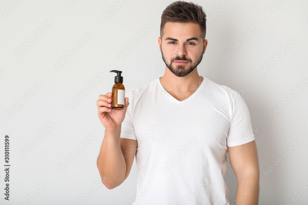 Handsome young man with cosmetic product on light background