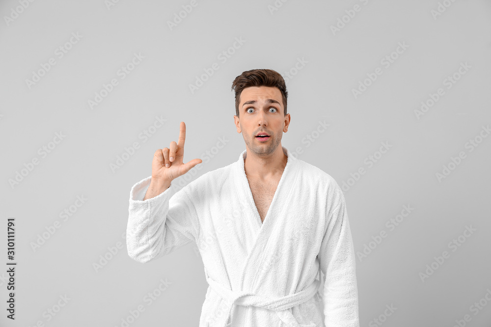 Surprised man in bathrobe pointing at something on grey background