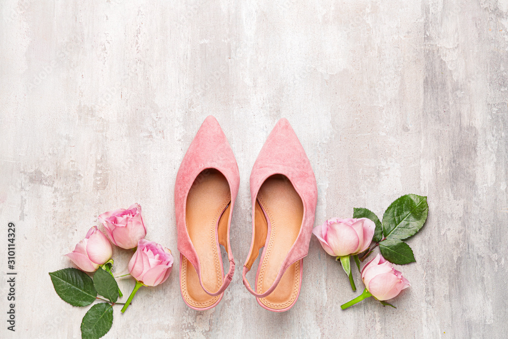 Stylish female shoes and flowers on light background