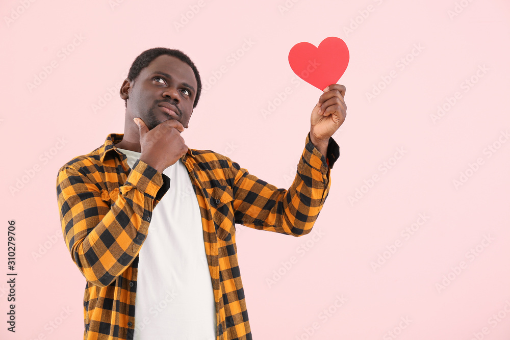 Thoughtful African-American man with red heart on color background