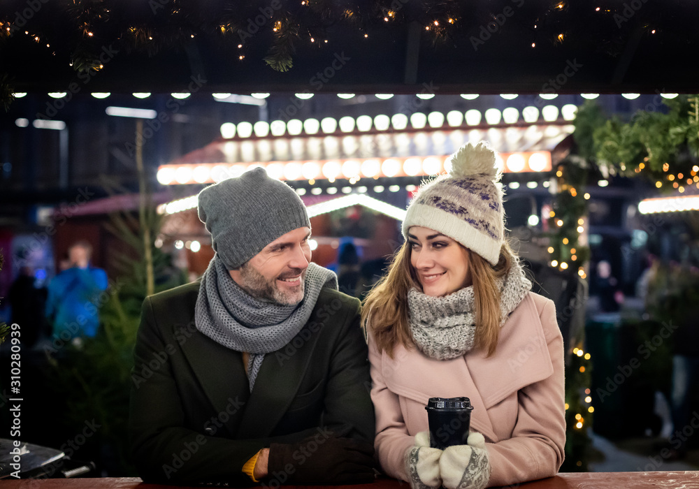 Loving couple visits the decorated Christmas market during the evening