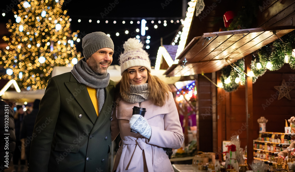 Loving couple visits the decorated Christmas market during the evening