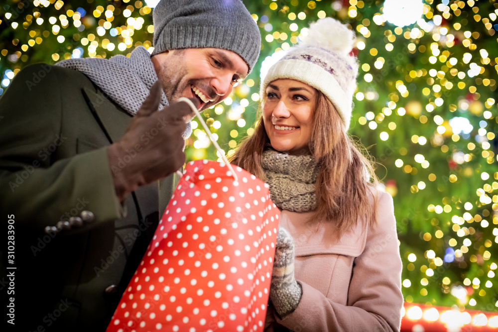 The couple give Christmas gifts against the background of outdoor decorations during an evening walk