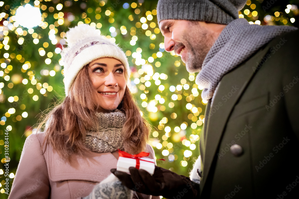 The couple give Christmas gifts against the background of outdoor decorations during an evening walk