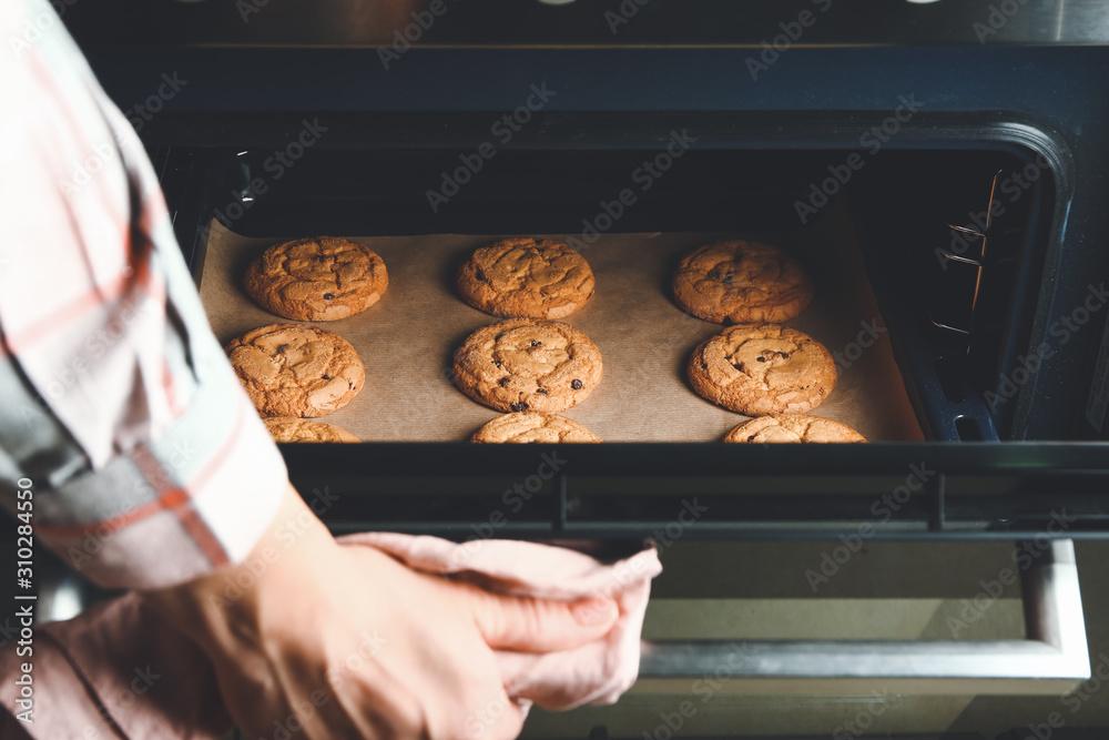 Woman taking baking tray with cookies out of oven