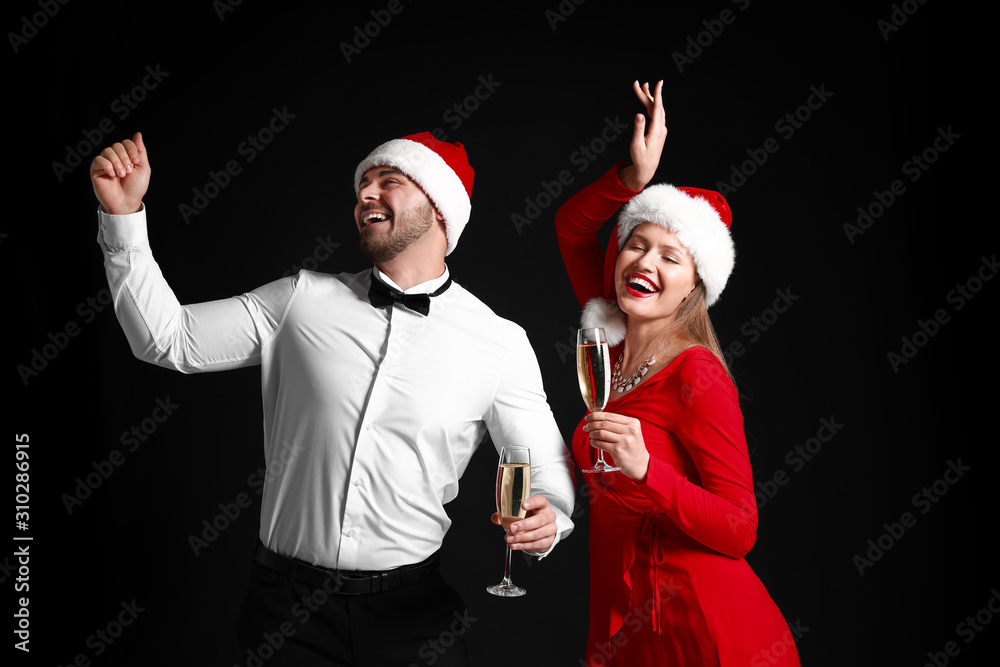 Happy couple in Santa Claus hats and with glasses of champagne on dark background