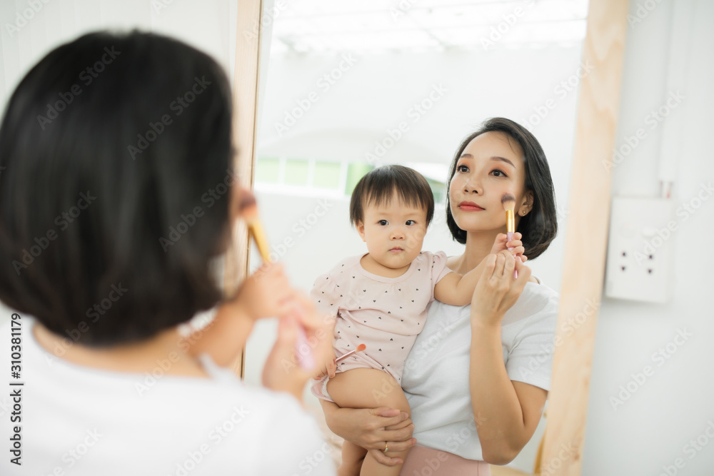 Funny family at home. Mother and her child girl are doing your makeup and having fun near mirror. Ba